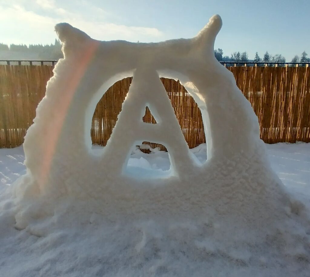A snow sculpture of an anarchist symbol with a lovely sun reflection