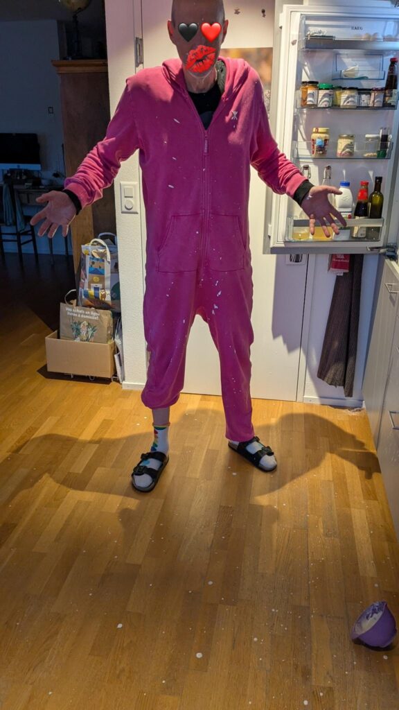 A man in a pink onesie has heart images on his face and cream splattered all over