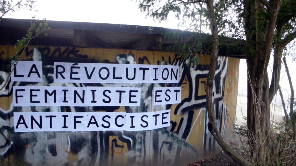 A wall next to a tree with a feminist collages that reads: La revolution feministe est antifasciste, the feminist revolution is antifascist