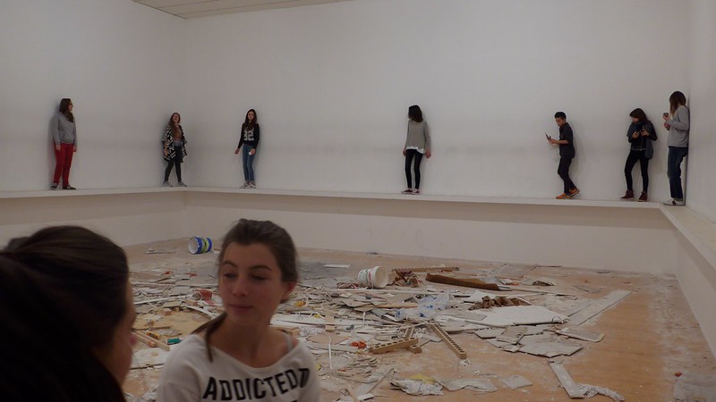 A group of teenagers balances on a ledge around some art work, in the front one wears a t-shirt that reads Addicted