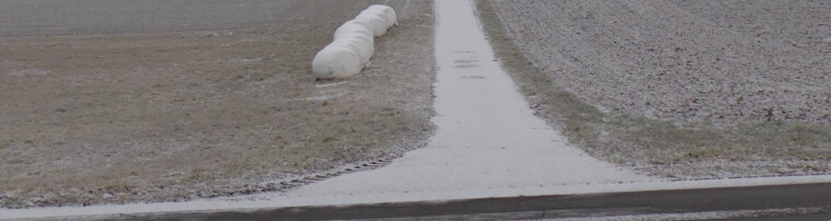 A road and a field with barely any snow and some white plastic balls